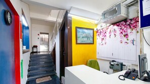 A hotel reception area with a staircase, a reception desk, a telephone, and a wall-mounted air conditioning unit. - FabHotel Saket Inn (Bhopal)