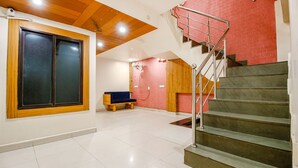 A spacious room with a large window, a bench, and a staircase leading to an upper level. - Fabexpress Sunshine Regency (Bhopal)