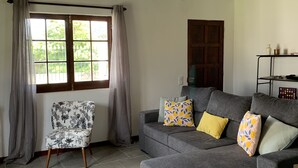 Een woonkamer met een grijze bank, een fauteuil met een patroon en een plafondventilator.