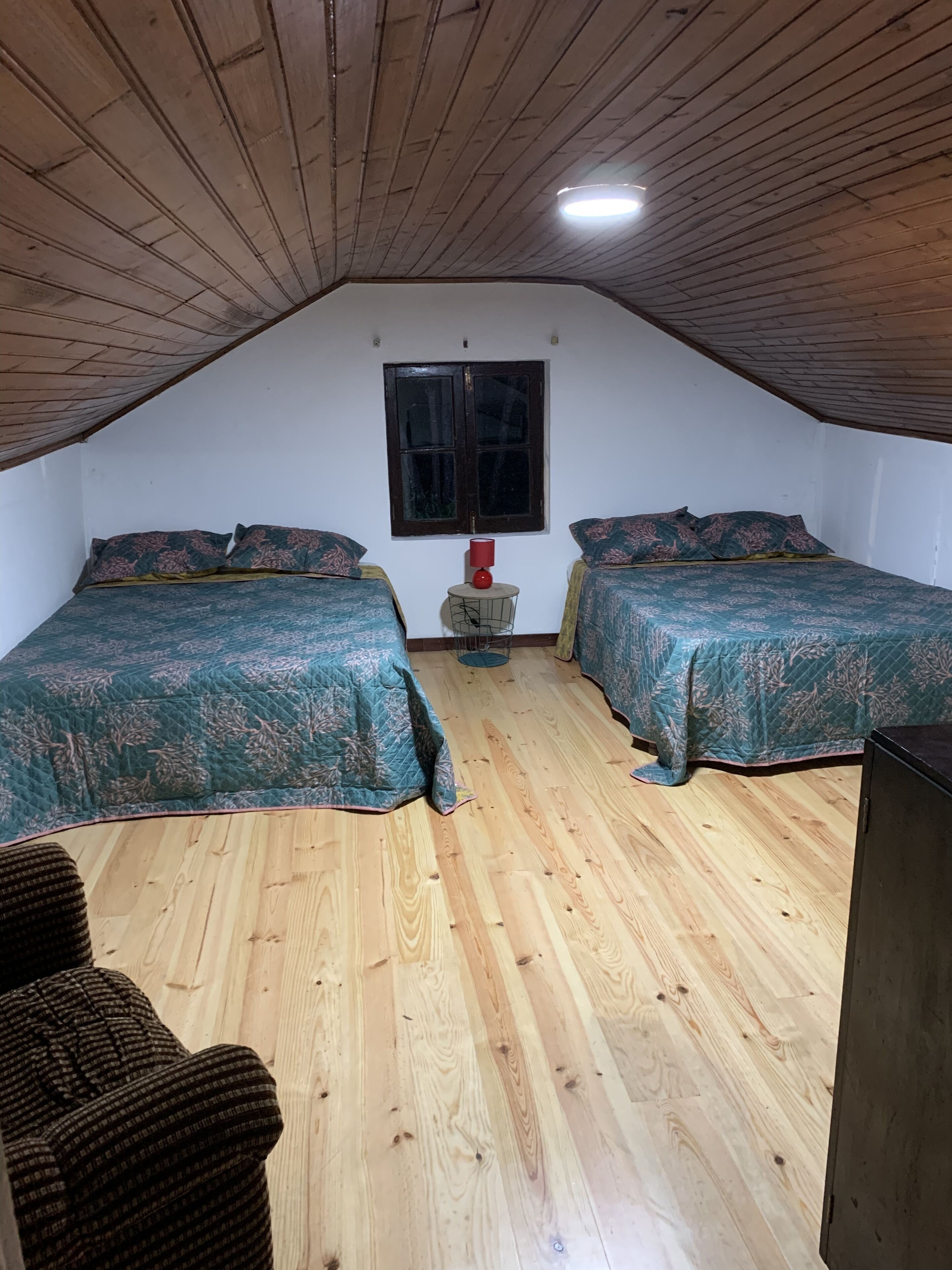 Une chambre avec deux lits, une petite table avec une lampe, une fenêtre et un ventilateur de plafond.