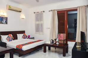 A hotel room with a bed, bedside table, TV, and a window with curtains. - FabHotel Premium- 10min Walk from Millennium City Centre Gurugram Gurgaon (Gurugram)
