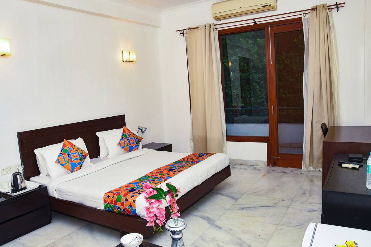 A hotel room with a bed, nightstands, a desk, and a window with curtains.