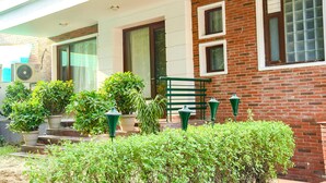 A building with a brick facade, multiple windows, and a covered porch area with potted plants and outdoor lighting. - FabHotel Premium- 10min Walk from Millennium City Centre Gurugram Gurgaon (Gurugram)