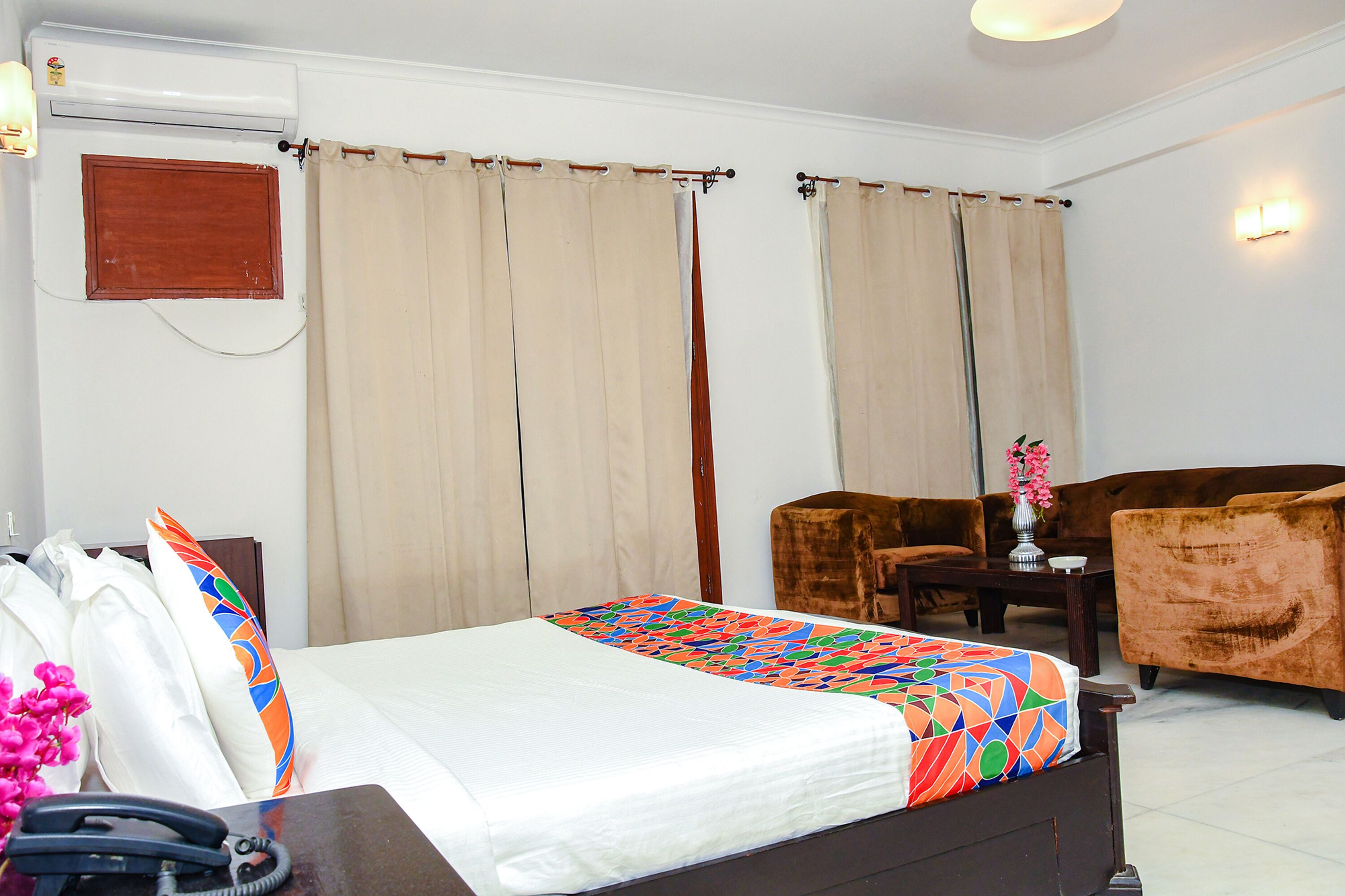 A hotel room with a bed, a sofa, a small table with a vase, and a telephone on a desk.