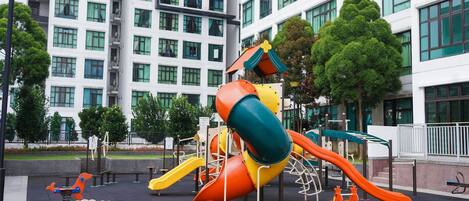 A playground with slides and swings, surrounded by a building with multiple windows and a white facade.