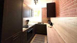A compact kitchen with dark cabinetry, a wooden countertop, a built-in oven, and a brick wall. - Dans la forêt de Pin by Interhome (Arcachon)