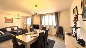 A modern living room with a dining area, a sofa, a chandelier, and a TV. - Dans la forêt de Pin by Interhome (Arcachon)