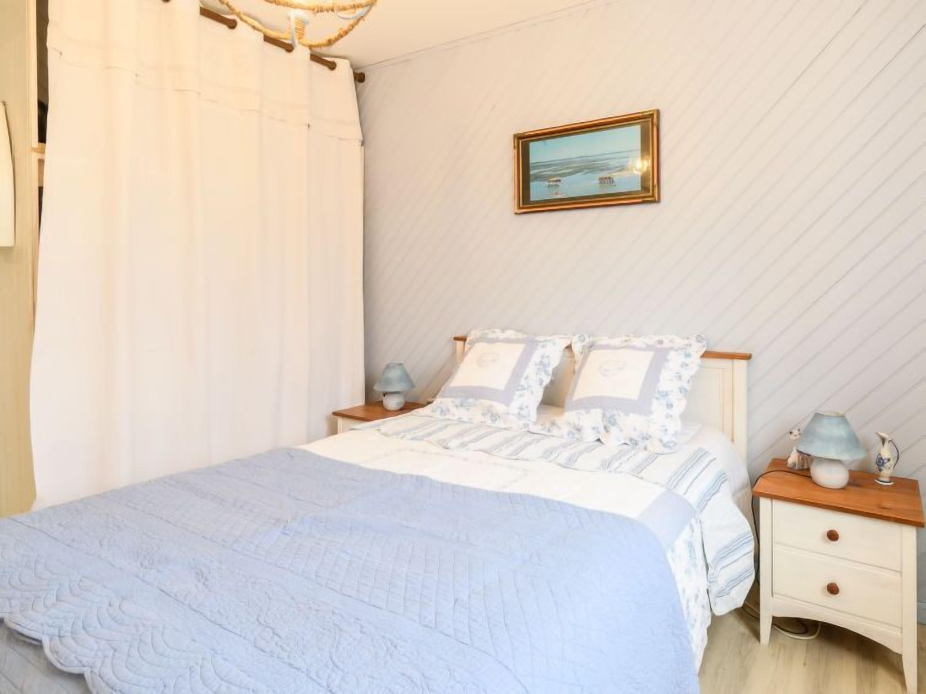 A bedroom with a bed, nightstands, a lamp, and a framed picture on the wall.