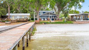 A waterfront property with a wooden dock, a house with a porch, and a large tree with Spanish moss.