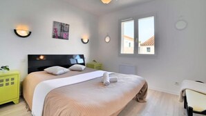 Un dormitorio con cama, mesitas de noche, ventana e iluminación en la pared.