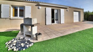Una casa de un piso con garaje, un patio con mesa de piedra y un pequeño jardín.