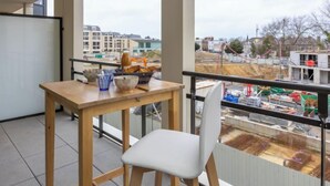 Een balkon met een houten tafel en stoelen, met uitzicht op een bouwplaats en woongebouwen.