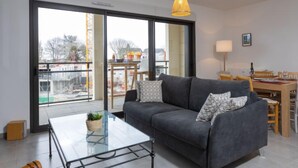 Een moderne woonkamer met een grijze bank, een glazen salontafel en een eetgedeelte met houten meubels.