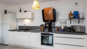 Een moderne keuken met witte kasten, een zwart aanrecht, een inbouwoven, een koffiezetapparaat en een magnetron.