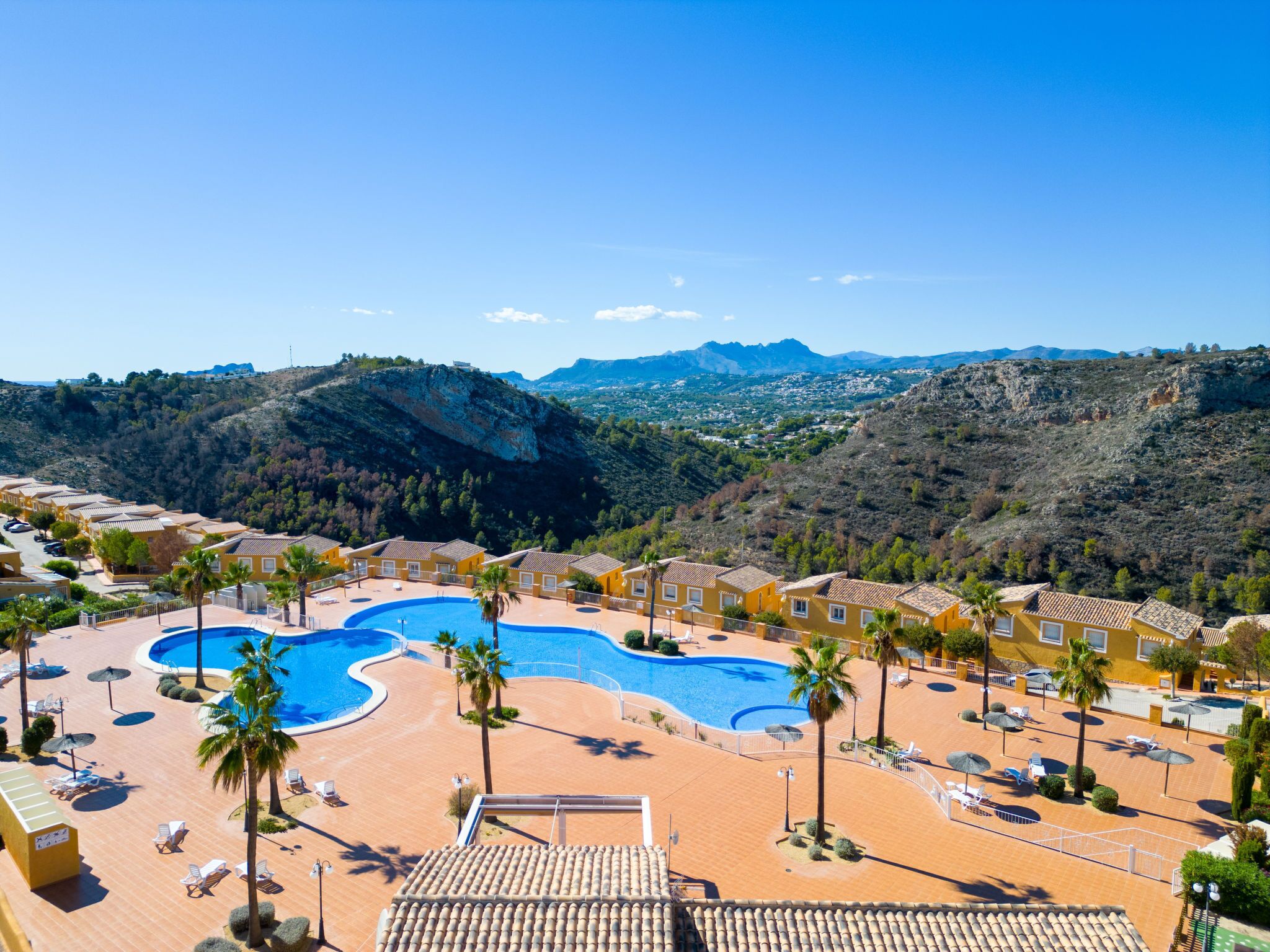 Um resort com uma piscina grande, palmeiras e montanhas ao fundo.