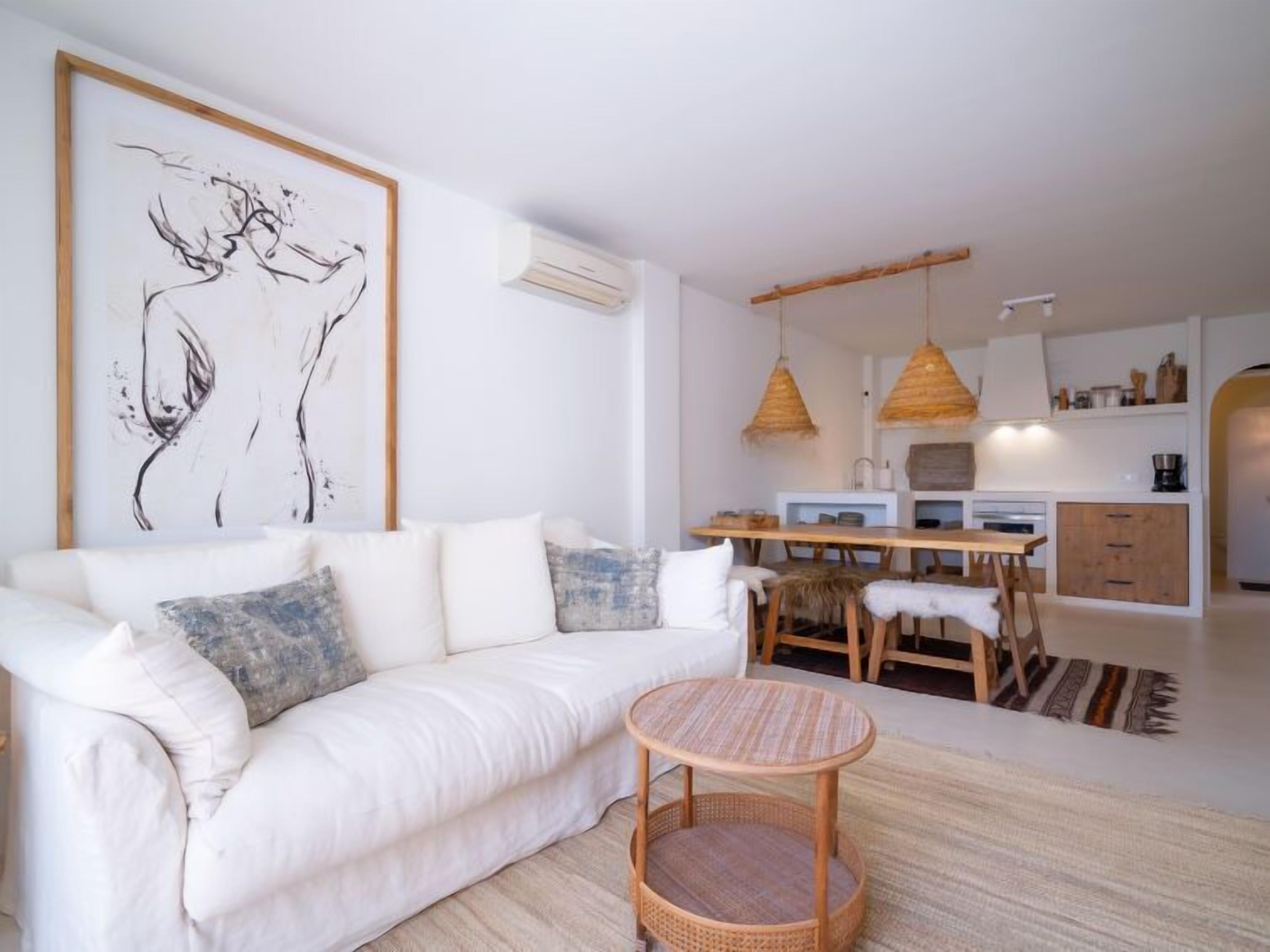 A modern living room with a white sofa, a round wicker table, and a dining area with wooden chairs and a hanging light fixture.
