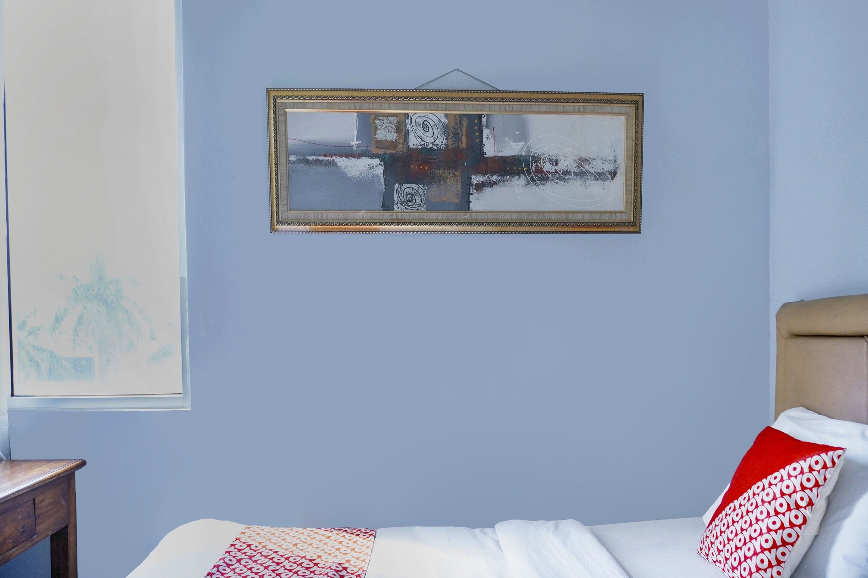 Une chambre à coucher avec un lit, une œuvre d’art encadrée au mur et une fenêtre donnant sur des arbres.