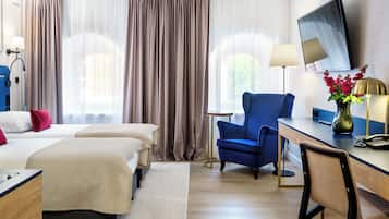 Quarto de hotel com duas camas, uma escrivaninha, uma cadeira, uma televisão e um vaso com flores.