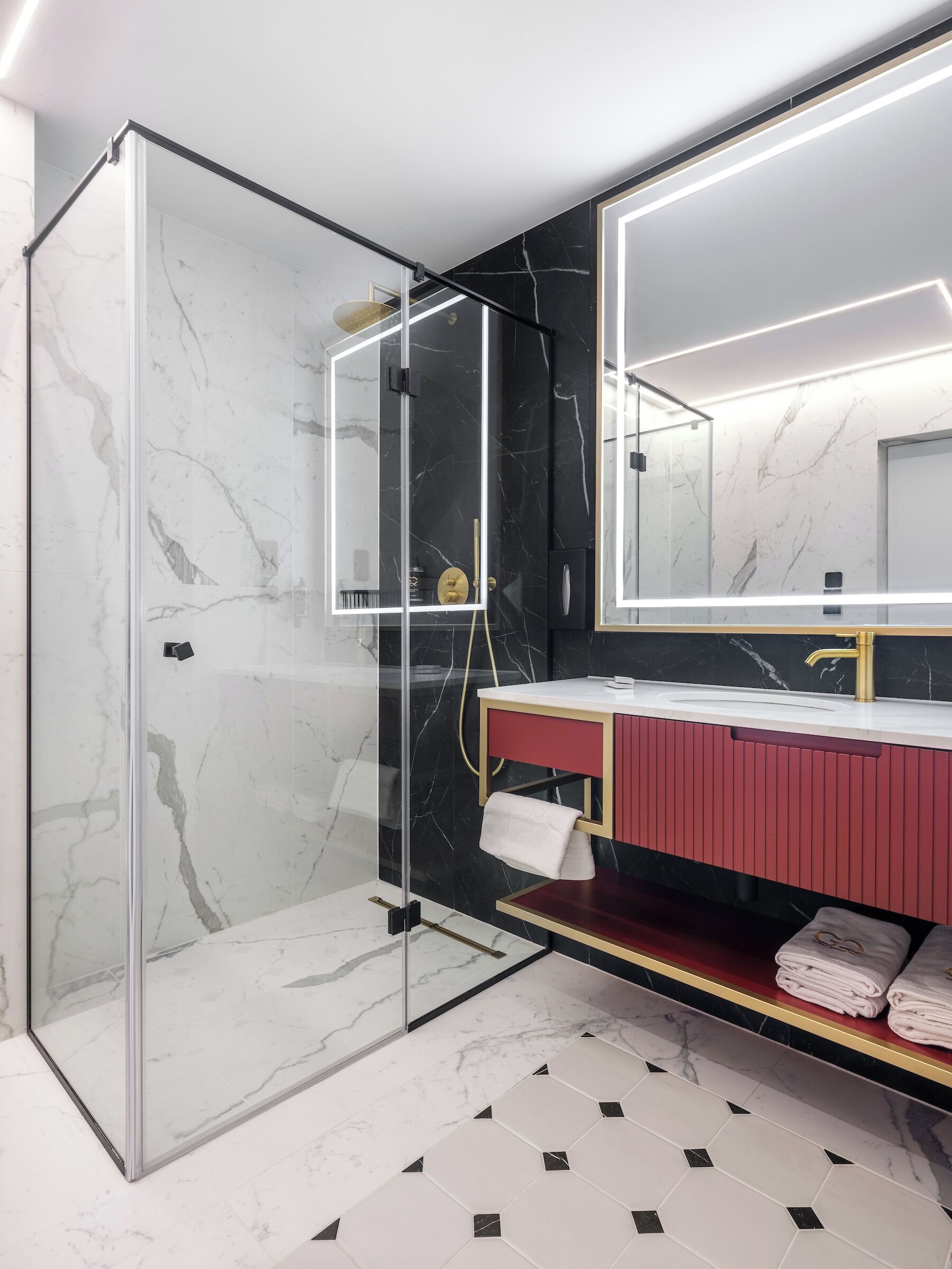 Un baño moderno con ducha envuelta en vidrio, tocador con gabinete rojo y un espejo grande.