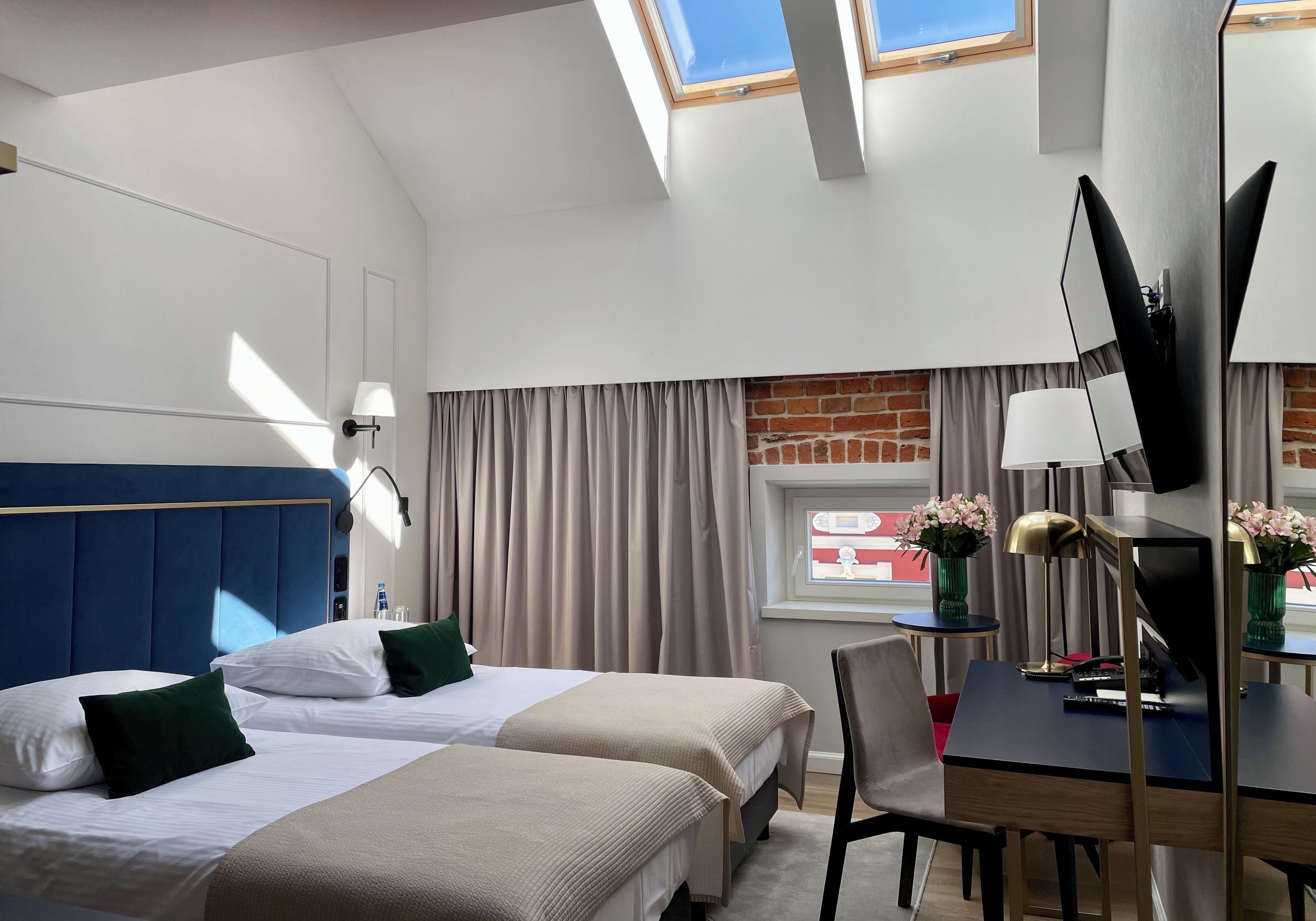 A hotel room with two beds, a desk, a chair, a TV, and a window with curtains.