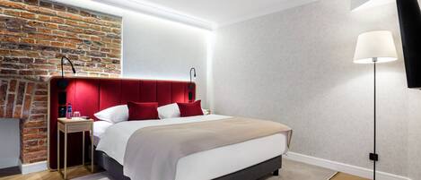 A modern bedroom with a brick accent wall, a red upholstered headboard, a bedside table with a lamp, and a floor lamp.