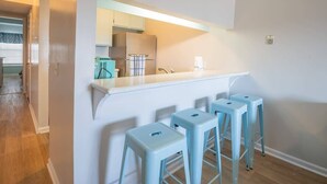 Uma cozinha com bancada branca, quatro banquetas azuis e uma geladeira de aço inoxidável.