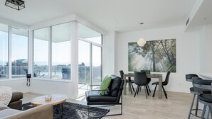 Ein modernes Wohnzimmer mit großem Fenster, einem Essbereich und einem Baumgemälde.