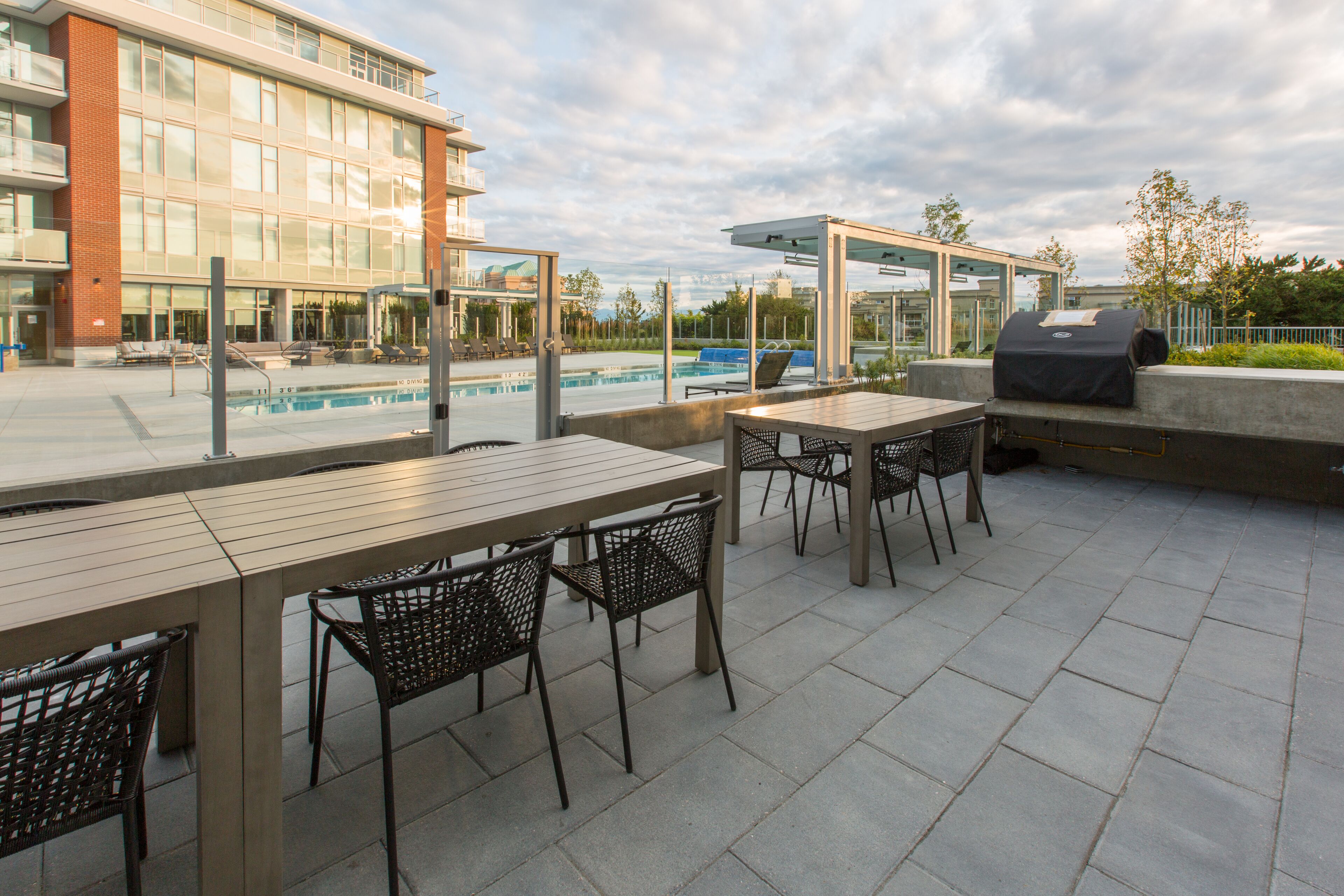 An outdoor patio with a pool, a covered grill area, and a seating arrangement with tables and chairs.