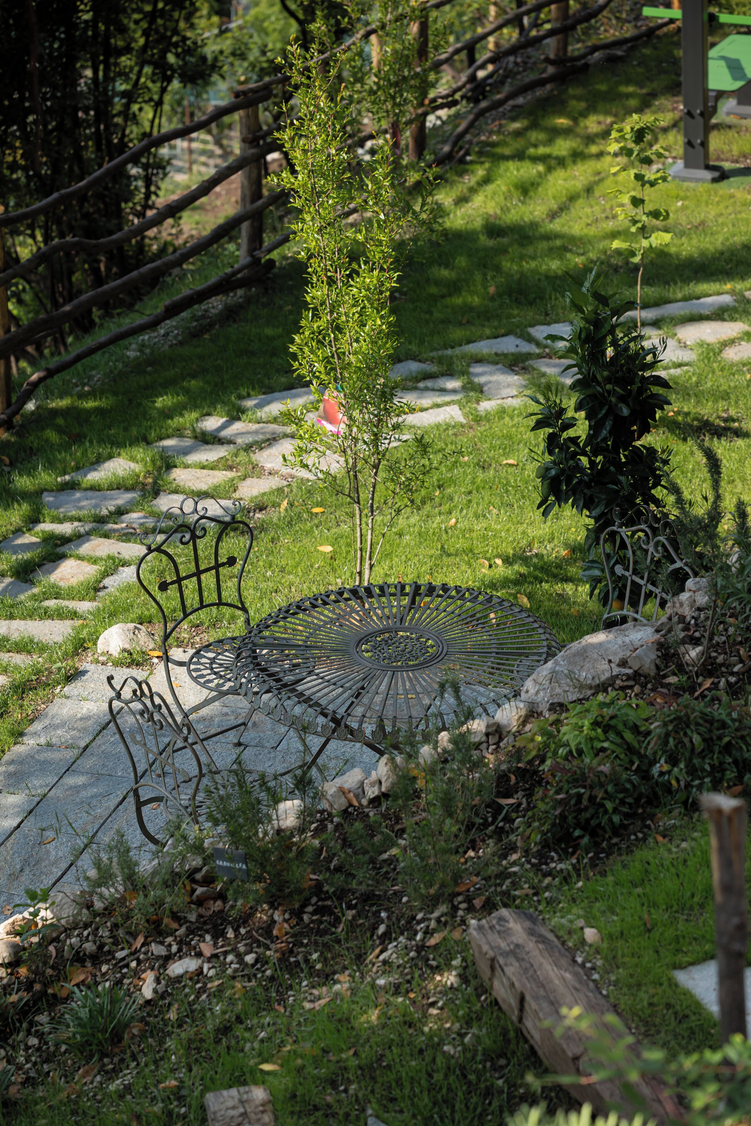 Ein Garten mit einer Metallbank, einem kleinen Baum und einem gepflasterten Weg.