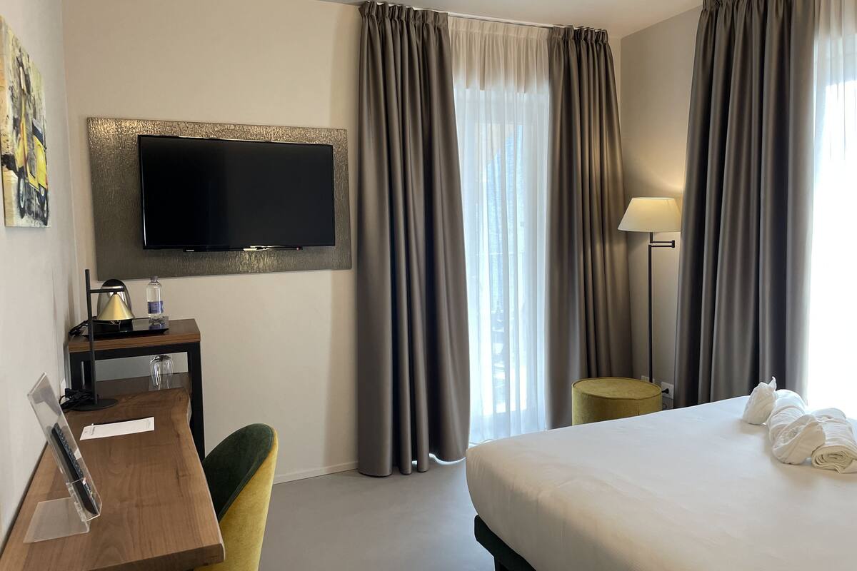 Ein Hotelzimmer mit Bett, Schreibtisch, Fernseher und Vorhängen.