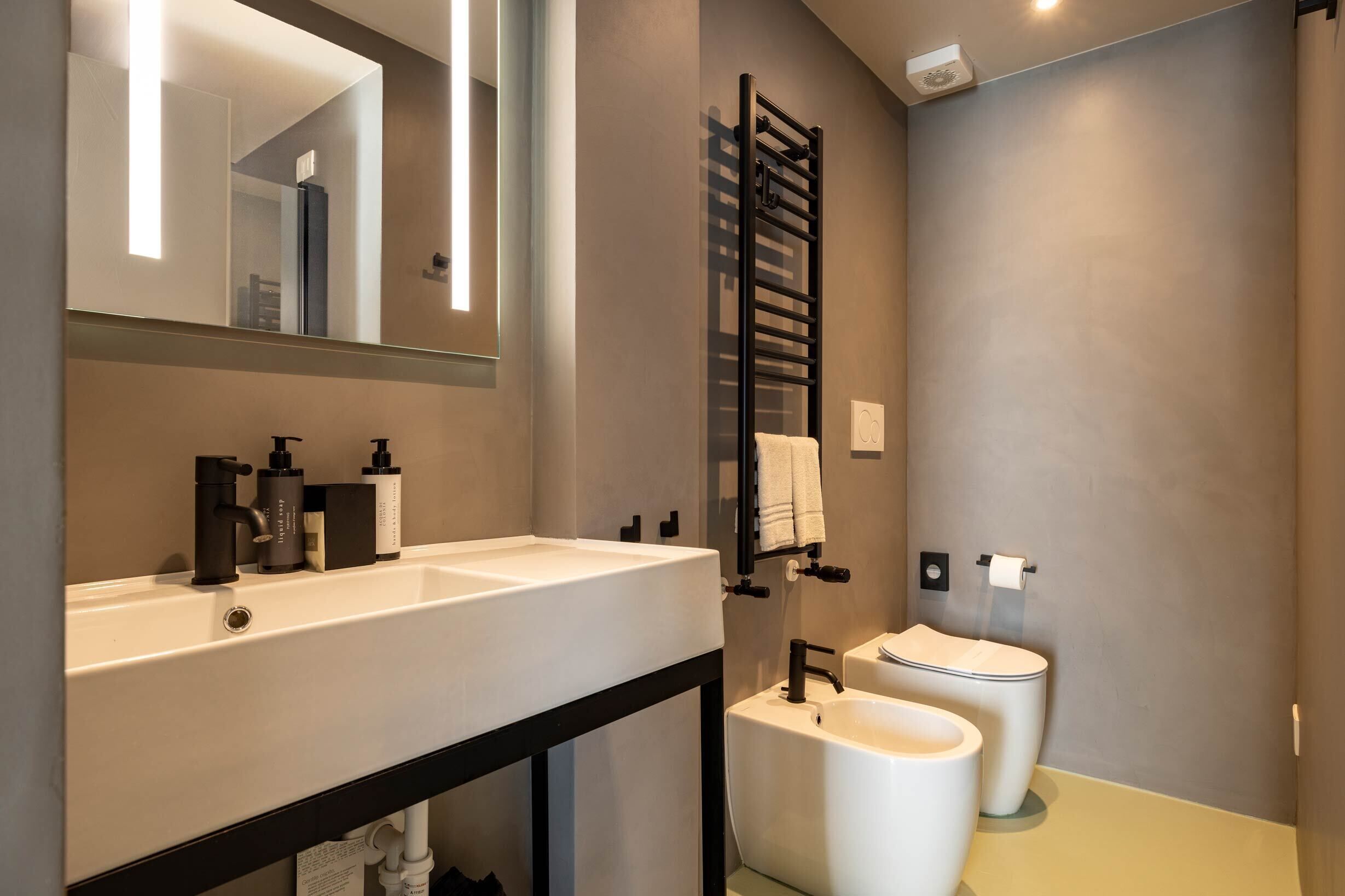 Une salle de bain moderne avec un meuble-lavabo à deux vasques, un porte-serviettes, des toilettes et un miroir.