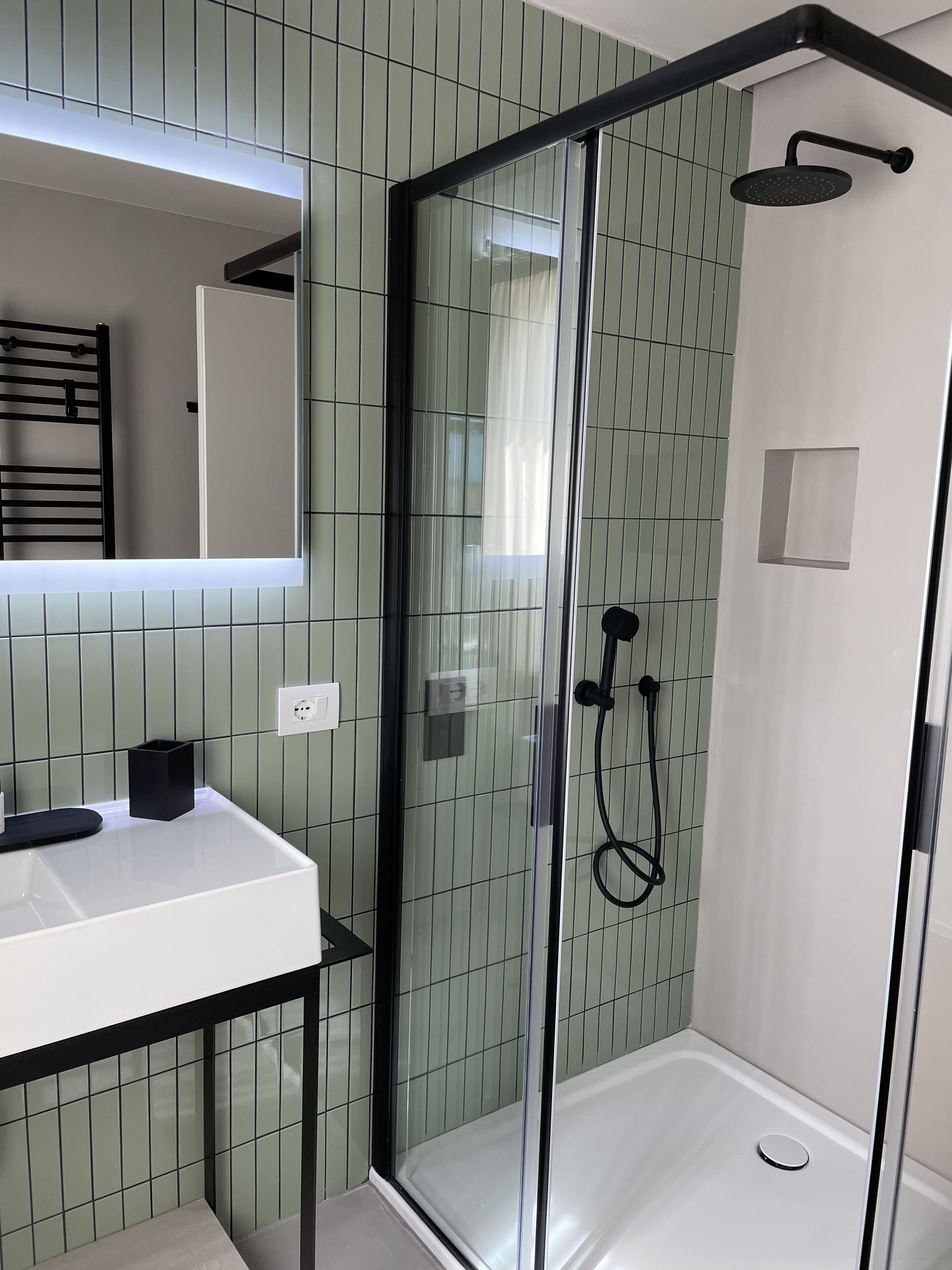 Un baño moderno con ducha acristalada, lavamanos blanco y un espejo sobre él.