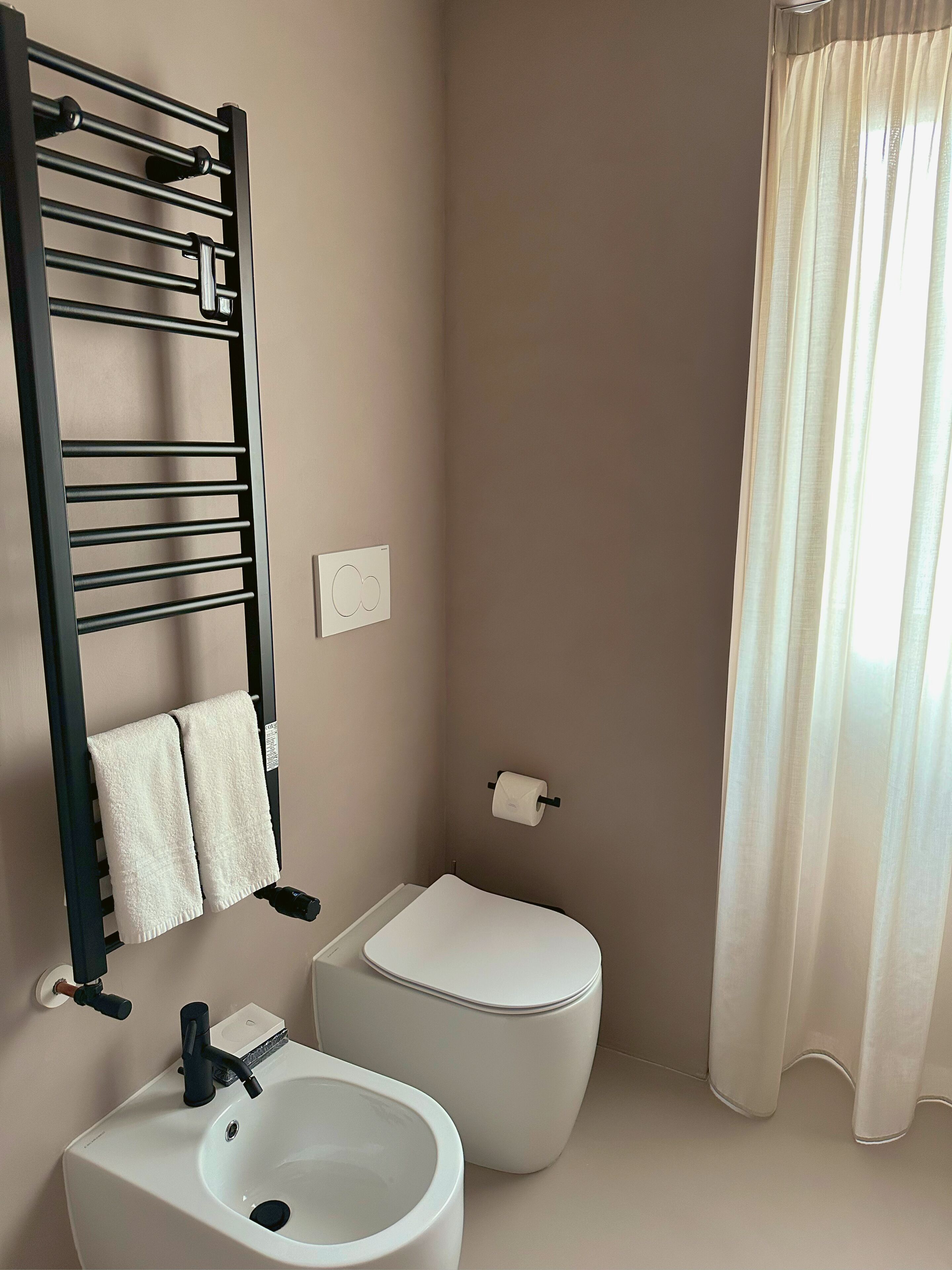 Un bagno moderno con un portasciugamani nero, un lavandino bianco, un water e una tenda da doccia.