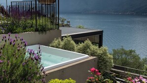 A modern outdoor pool area with a view of a lake and mountains, surrounded by lush greenery and flowers. - Villa Clementina Boutique Hotel (Colonno)