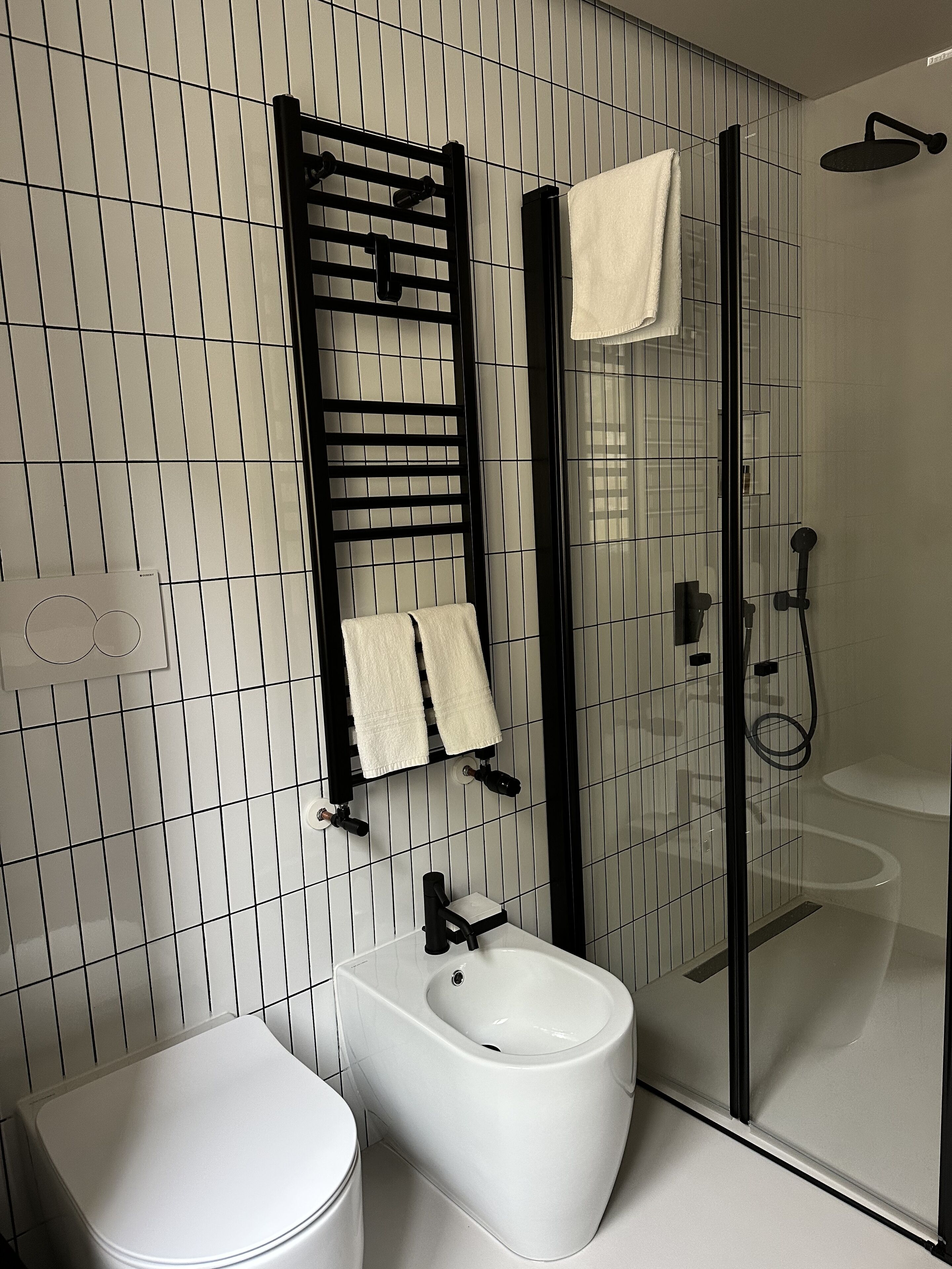 A modern bathroom with a bidet, a toilet, a glass-enclosed shower, and a towel rack with two towels.