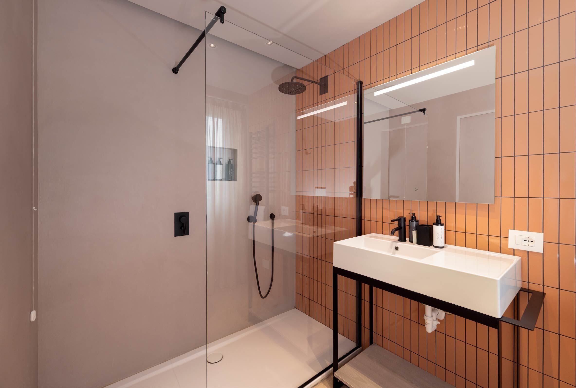 Un bagno moderno con doccia vetrata, un lavandino bianco con elementi neri e uno specchio sopra al lavandino.