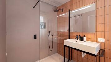 Un bagno moderno con doccia vetrata, un lavandino bianco con elementi neri e uno specchio sopra al lavandino.
