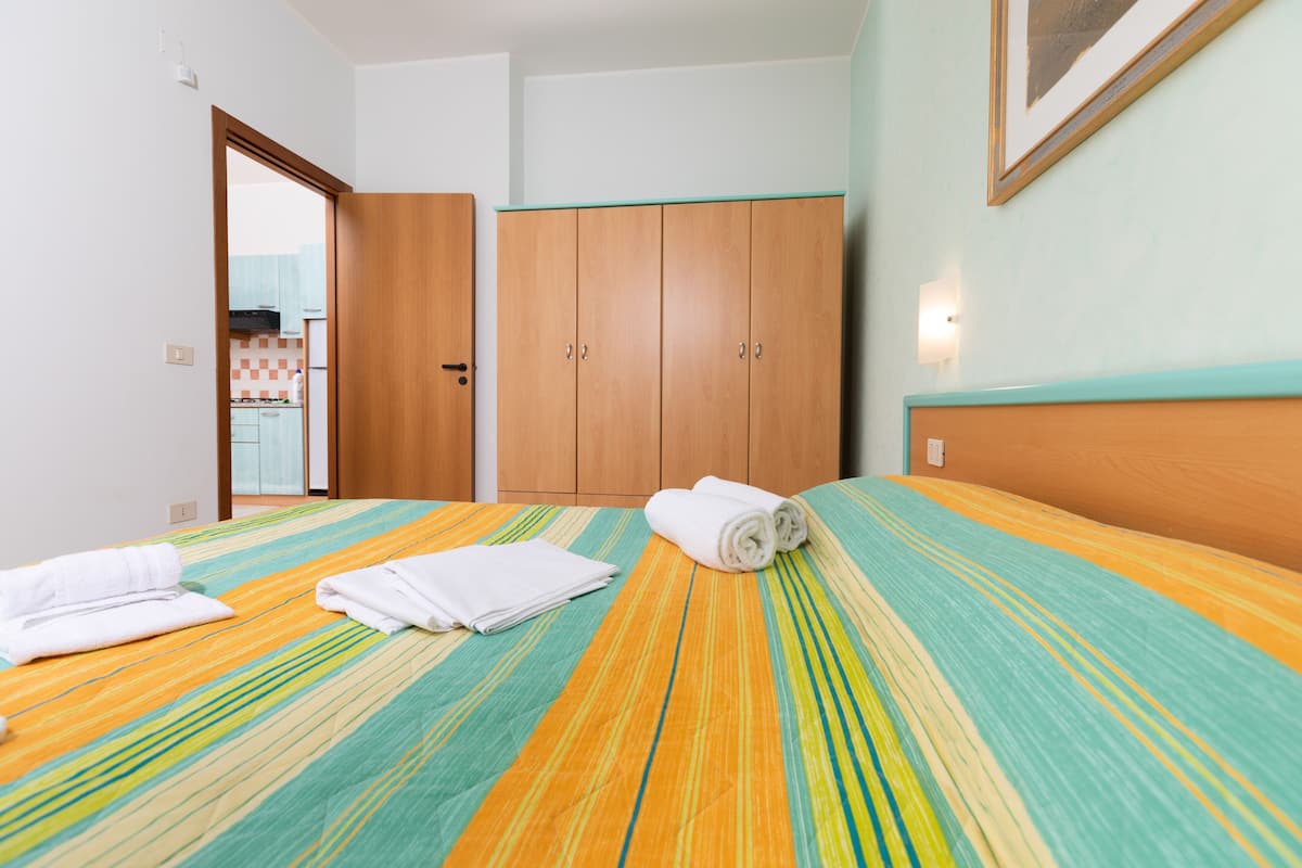 Quarto de hotel com cama, guarda-roupa de madeira e banheiro visível através de uma porta aberta.