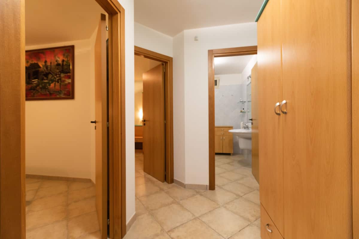 Um corredor com um guarda-roupa de madeira, um quadro na parede e um banheiro visível por uma porta aberta.
