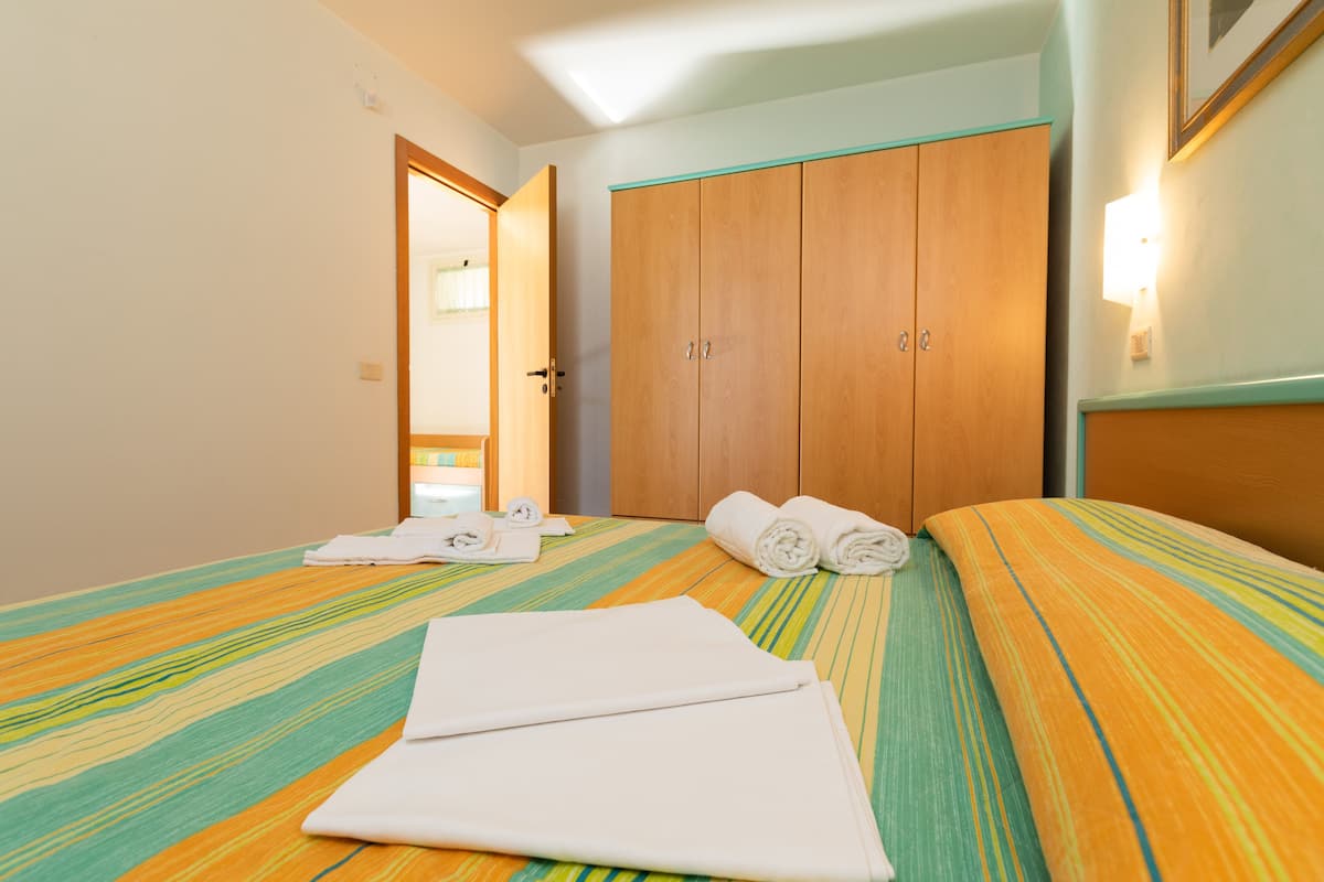 Quarto de hotel com uma cama, um guarda-roupa de madeira e uma casa de banho visível através de uma porta aberta.