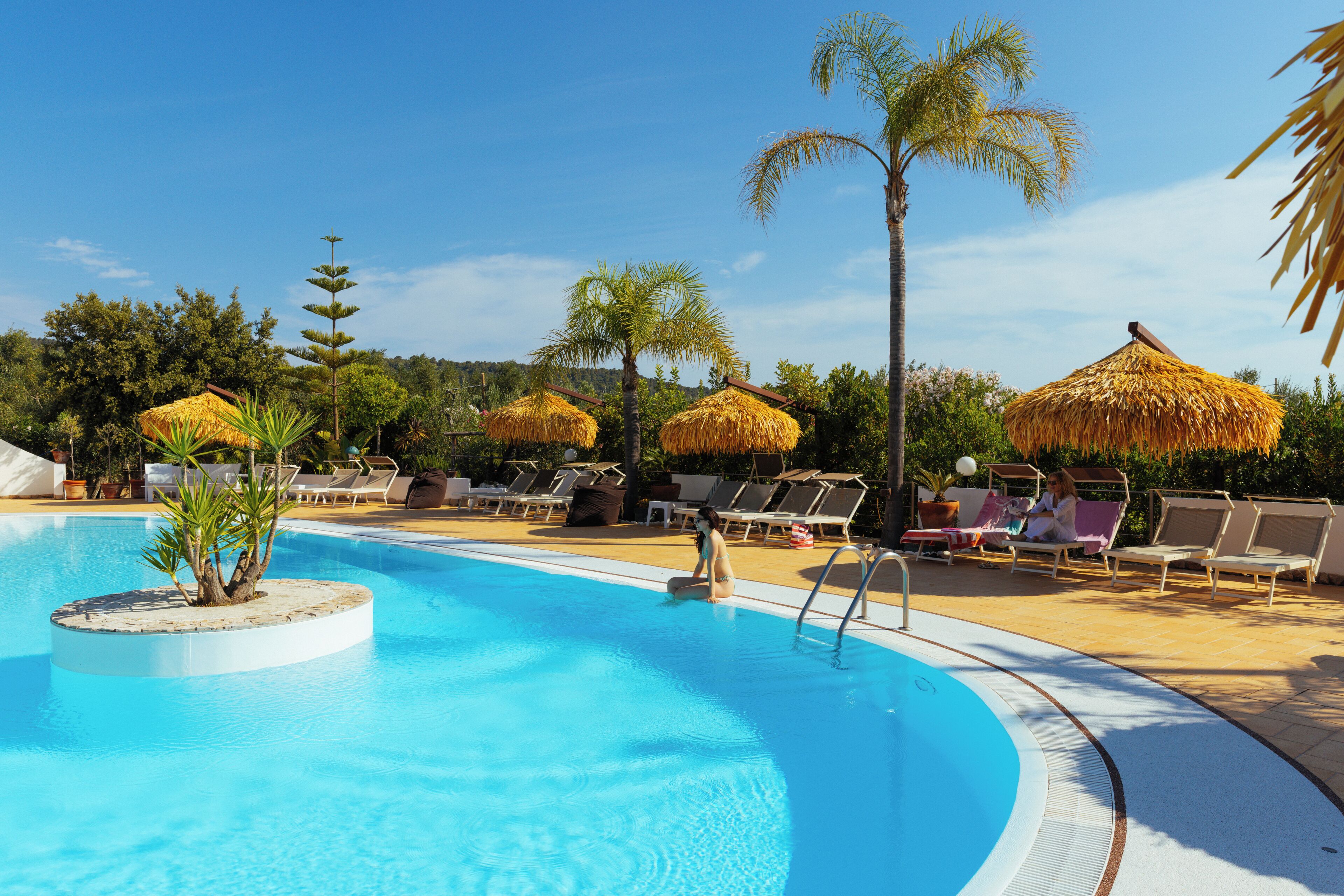 Una piscina con lettini e palme.