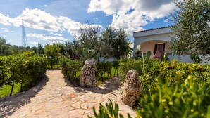 A stone pathway leading to a building with a red door, surrounded by greenery and a clear sky. - Residence Villantica (Vieste)