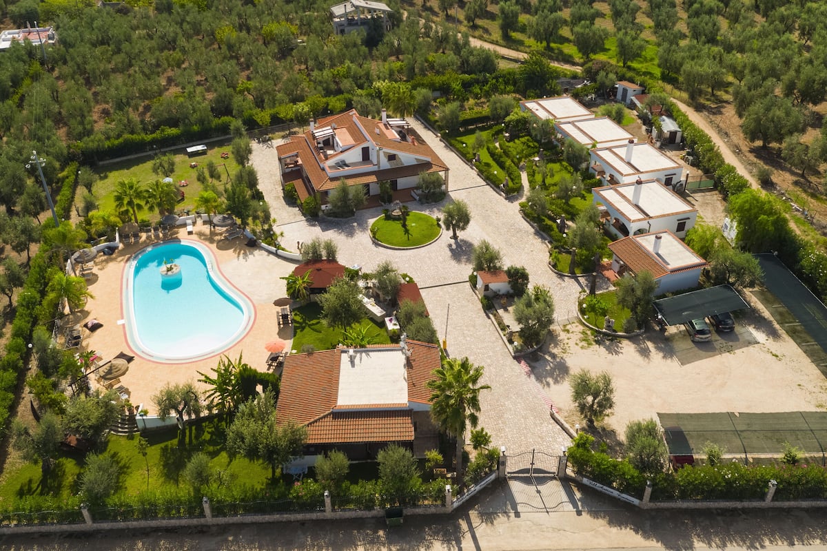 Vista aérea de um resort com piscina, várias villas e jardins bem cuidados.