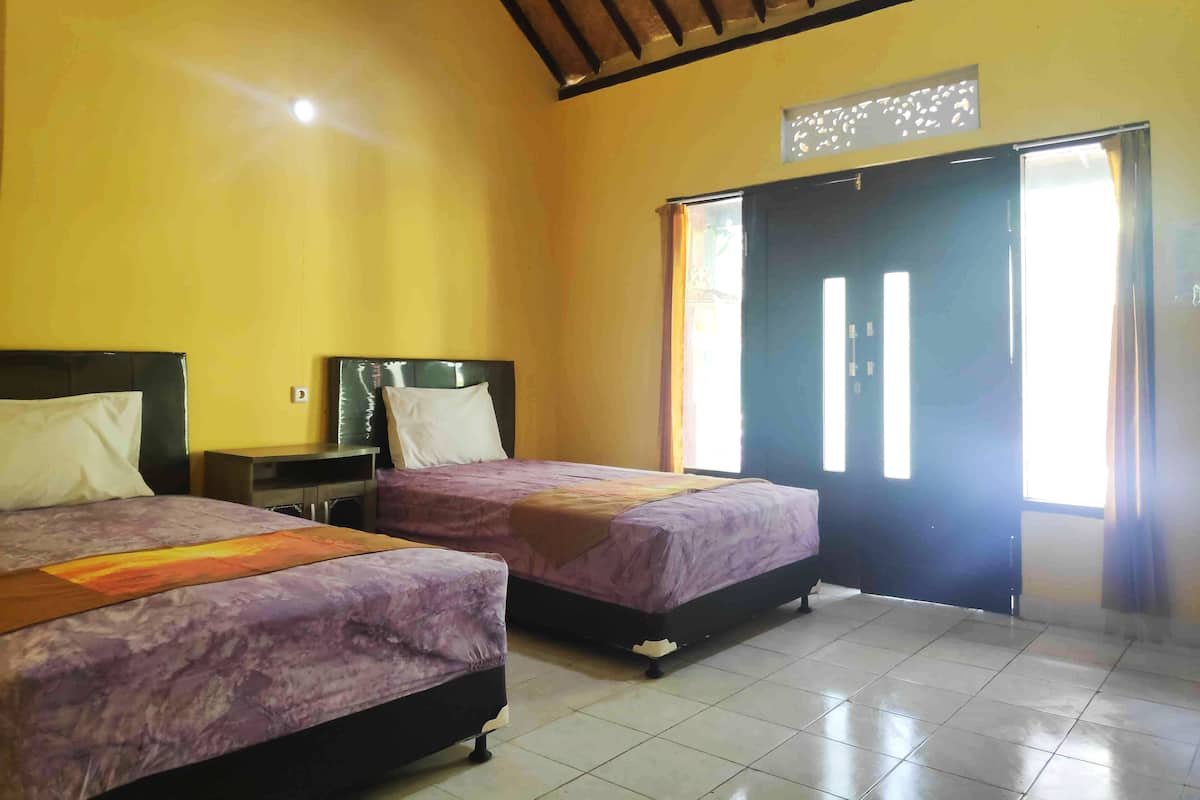 Une chambre avec deux lits, un plafond en bois, un sol carrelé et une porte avec une fenêtre.