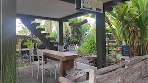 Ein Terrassenbereich im Freien mit einem Holztisch und Stühlen, umgeben von üppigem Grün und einem hängenden Schild.