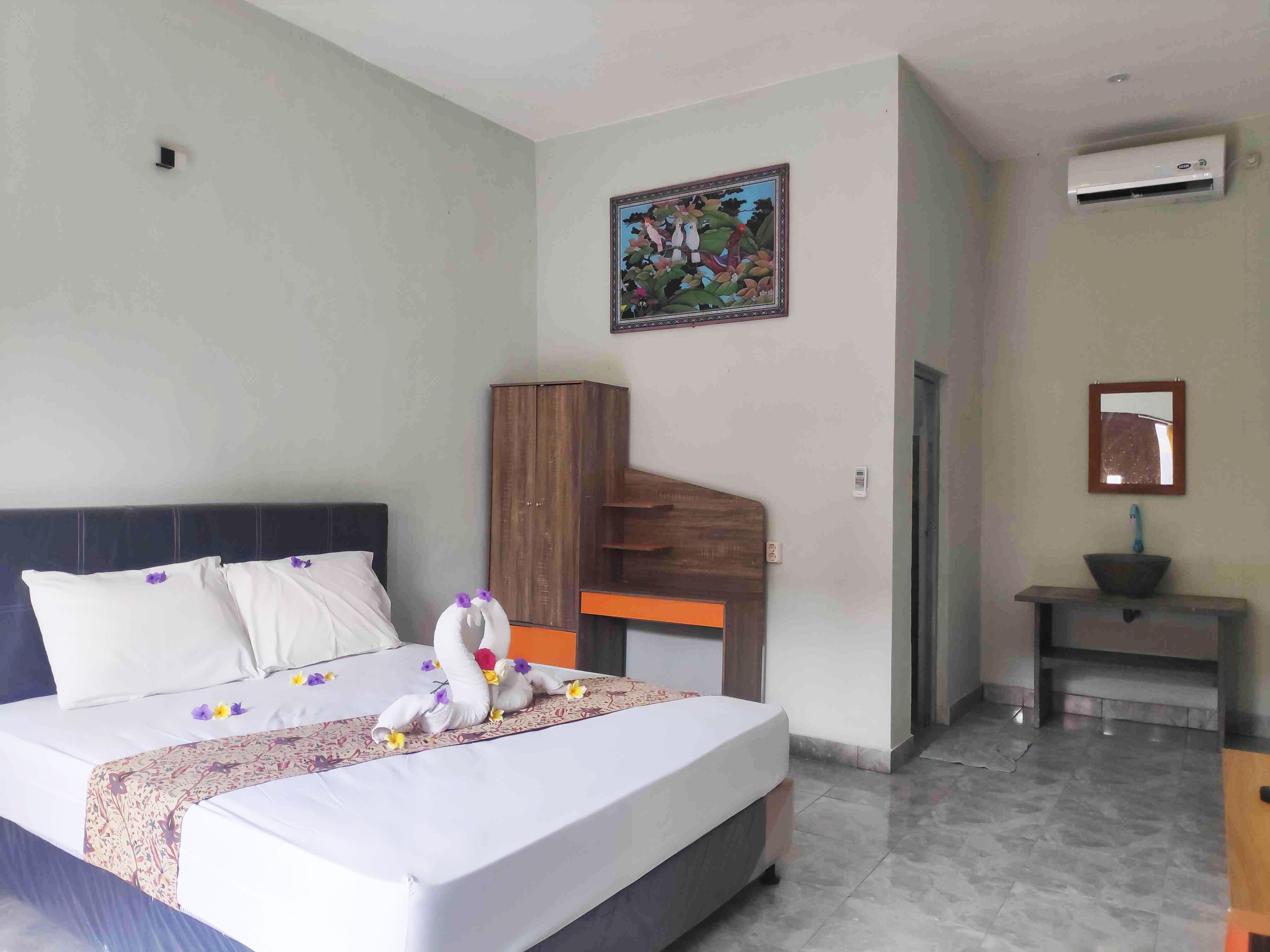 A hotel room with a bed, a wooden wardrobe, a bathroom with a sink and mirror, and an air conditioning unit.