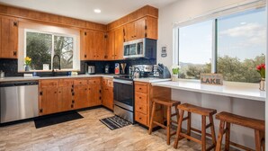 A modern kitchen with wooden cabinets, stainless steel appliances, a large window with a view of trees, and a sign reading "Welcome to the LAKE".