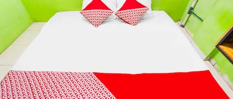 A bed with a white and red bedspread, two red pillows, and a green wall.