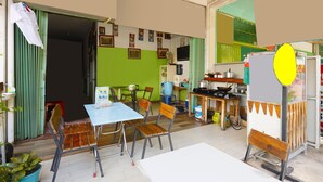 A dining area with a table and chairs, a kitchen area with cooking utensils, and a green wall with framed pictures. - Hotel O Wr House Syariah BatamNearEast Coast Park (Batam)