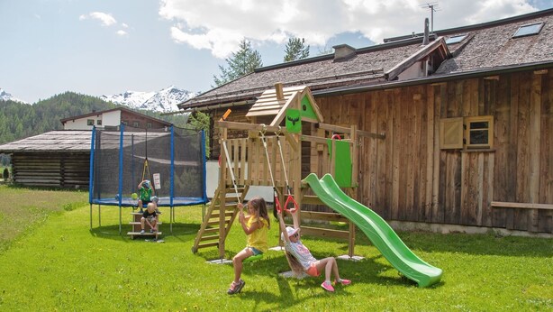 A wooden play structure with a slide, swings, and climbing elements in a grassy area. - Ihr Zuhause im Urlaub - Familiär und Komfortabel (Niederthai)